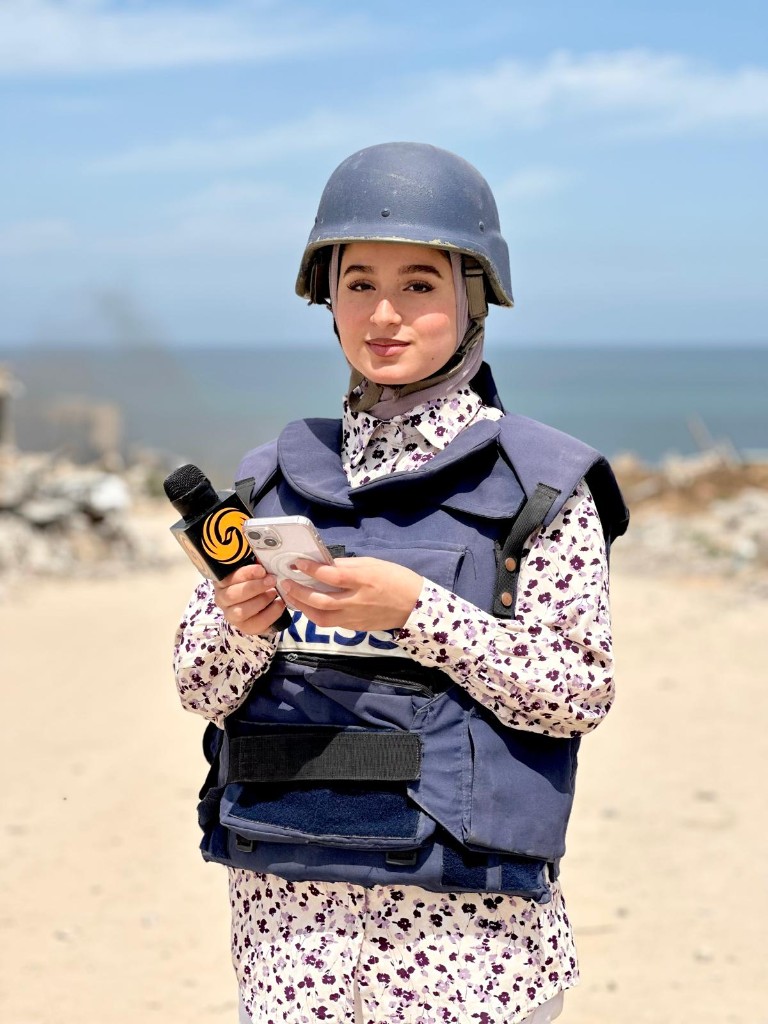 Nour Elassy in press gear, holding a microphone and her phone